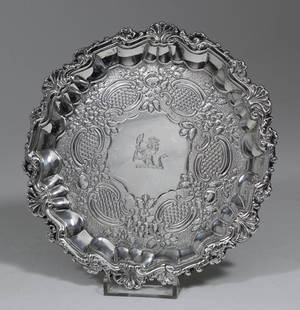 A late George III silver circular waiter of mid 18th: A late George III silver circular waiter of mid 18th Century design, the moulded rim with cast shell and scroll mounts, the centre engraved with flowers, C-scroll and scale ornament, on three leaf