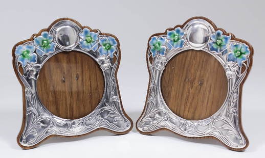 A matched pair of Edward VII silver and enamelled: A matched pair of Edward VII silver and enamelled photograph frames of shaped outline and of Art Nouveau design, decorated in green and blue with flowers and embossed with scrolled leafage, 7.5ins x