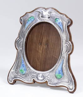 An Edward VII silver and enamelled photograph frame of: An Edward VII silver and enamelled photograph frame of shaped outline and of Arts & Crafts design decorated in green and blue with cabochon tear drop "Ruskins" on a planished inner border, 8ins x