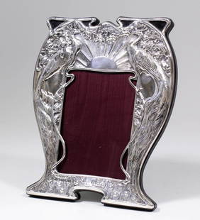 An Elizabeth II silver photograph frame of Art Nouveau: An Elizabeth II silver photograph frame of Art Nouveau design and of shaped outline, cast in relief with peacocks and with sunburst motif, 9ins x 7ins (to take picture 5ins x 3.5ins), by P.V.F.,
