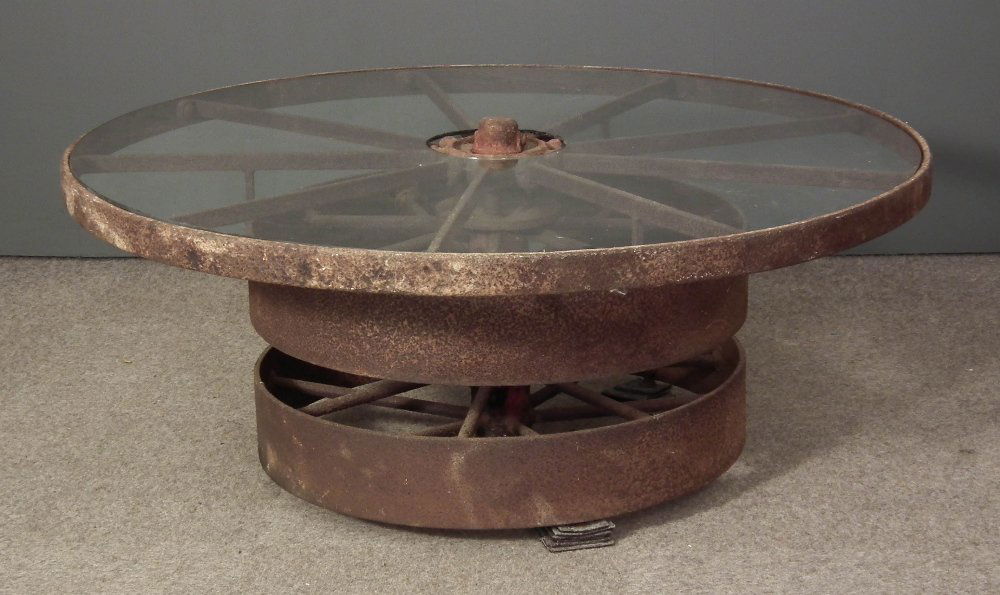 An unusual iron circular coffee table formed from three: An unusual iron circular coffee table formed from three old belt or pulley wheels, now with plate glass circular top, 47ins diameter x 19ins high (plate glass chipped at edges and metalware rusted) No