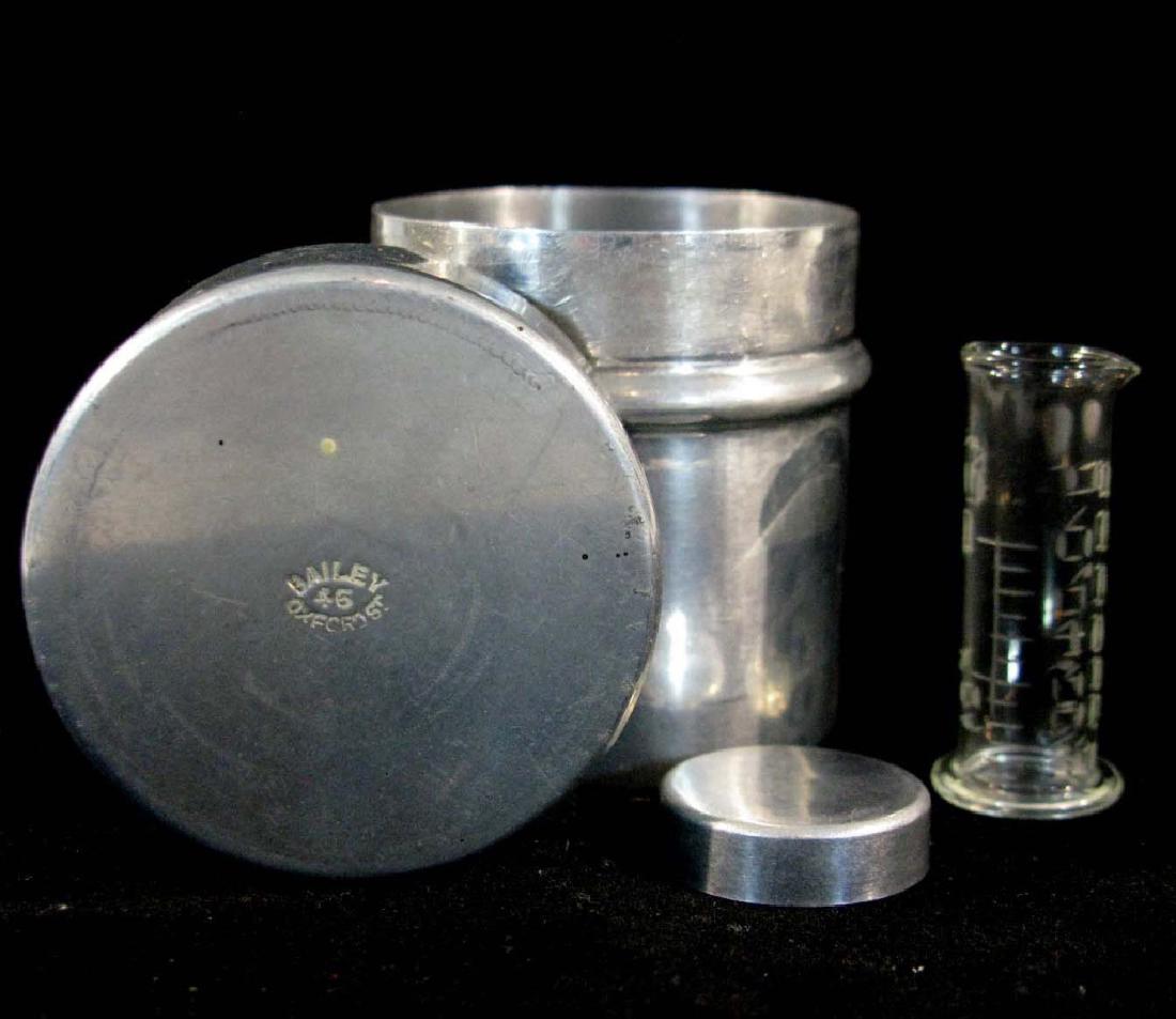 CHEMISTS MEASURE BAILEY 46 OXFORD ST: CHEMISTS MEASURE: Round, tin container containing a fitted cylinder into which a glass beaker is held with etched measurements, with a fitted lid. Lid impressed: BAILEY 46 OXFORD ST. 2.5"h.