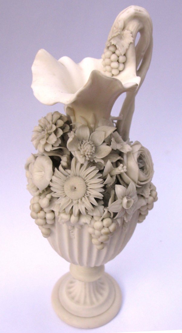 Parian Floral Wine Pitcher possibly Worcester: This is an antique parian ware wine pitcher with a shield shaped body and ruffled lip and twisted vine handle. The body has been encrusted with hand formed and placed flowers which include, daisies, r
