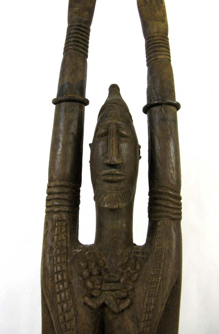 African Carved Wood Dogon Female Mali Figure: African Wood and metal Mali female figure shown with hands raised and children at her feet; metal bands around both raised arms. Figure depicted with both hands raised which can indicate a protection 