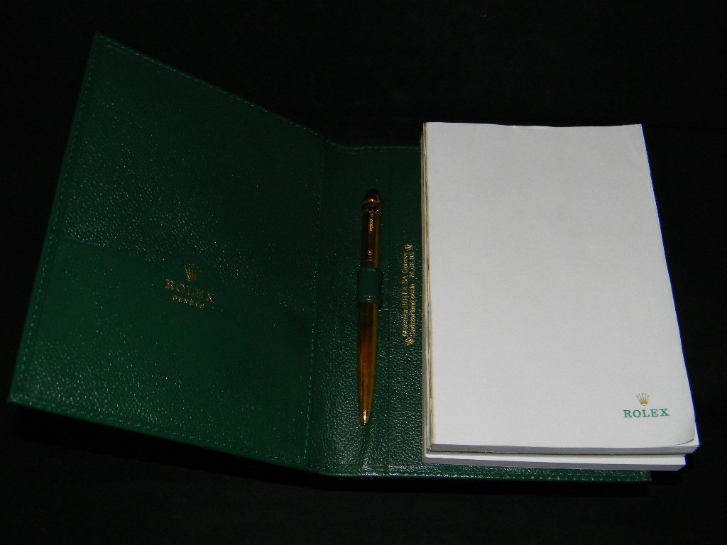 ROLEX GOLD PEN AND NOTEPAD STATIONARY SET: ROLEX GOLD PEN AND NOTEBOOK STATIONARY SET: The large pen is a gold-plated rollerball model with the Rolex name embossed on the base; this is housed in a green leather cover which includes three Rolex