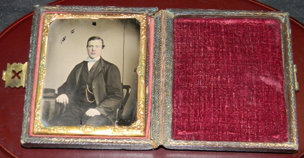 CIVIL WAR ERA AMBROTYPE IN PRESSED LEATHER CASE: CIVIL WAR ERA AMBROTYPE IN PRESSED LEATHER CASE: Depicting a well dressed young man in with a blue tinted bow tie and gold waist coat chain. housed in a pressed leather case with metal clasp. Plate me