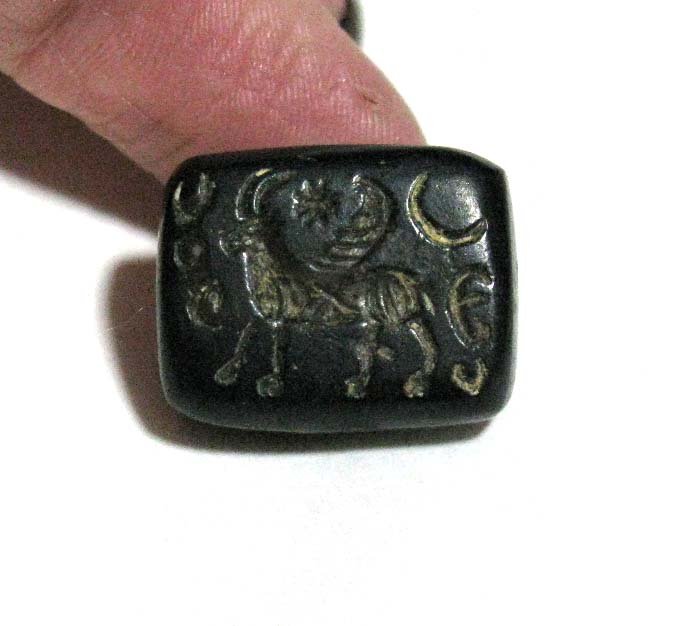 SYRIAN BLACK STEATITE SEAL: Animal Motif: SYRIAN BLACK STEATITE SEAL: A Syrian black steatite semi-spherical seal bead, depicting an two-horned, winged animal with crescent moon and star above, surrounded by archaic carvings, .75" l x .625" w