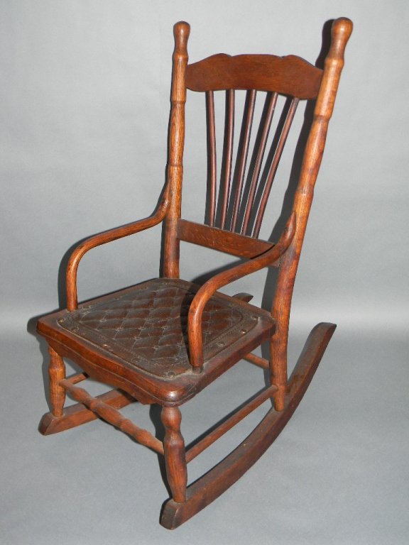 VICTORIAN WOODEN DOLL OR CHILD'S ROCKER: VICTORIAN WOODEN DOLL OR CHILDS ROCKER: Oak rocker with embossed leather seat over caned base, 28" h (71.12 cm).