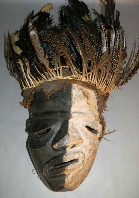 AFRICAN DANCED MBANGU SICKNESS MASK PENDE, CONGO: Danced African Carved Wood Mbangu (Sickness) mask, Pende, Congo with twisted face bisected by white and black pigments, Carved mouth, nose and eyes, and at edge adorned with bird feathers and burlap,