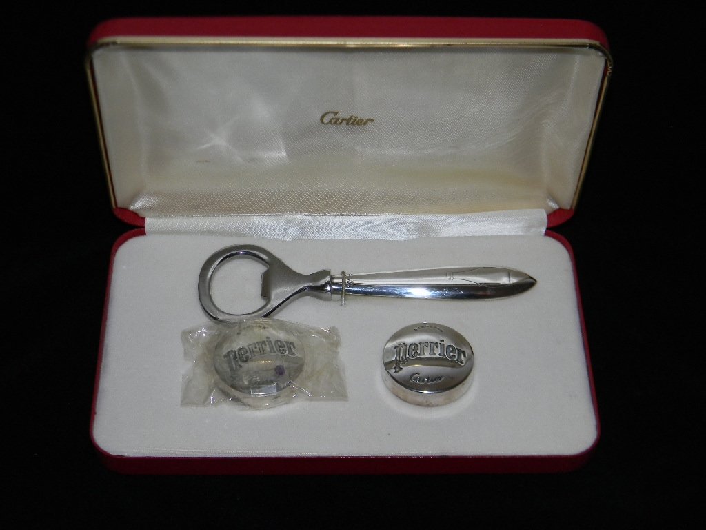 CARTIER STERLING BOTTLE SET FOR PERRIER: Cartier sterling silver bottle opener and two caps produced for Perrier Sparkling Water. Opener embossed with the image of a bottle and Cartier. Each Sterling cap with, Cartier and Perrier. Housed in 