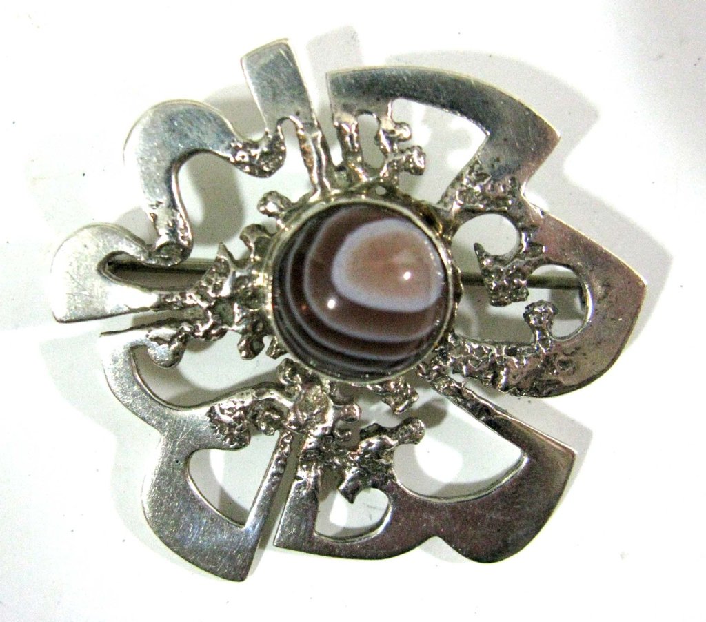 OLA M GORIE SCOTTISH PIN/BROOCH W/ AGATE CABOCHON: OLA M GORIE SCOTTISH PIN/BROOCH WITH AGATE: Ola M Gorie (b. 1937), Brooch in a brutalist, mid-century design which is mounted with a banded agate cabochon, 1.5"d, 14.91g, 9.59dwt., hallmarked OMG Ola 