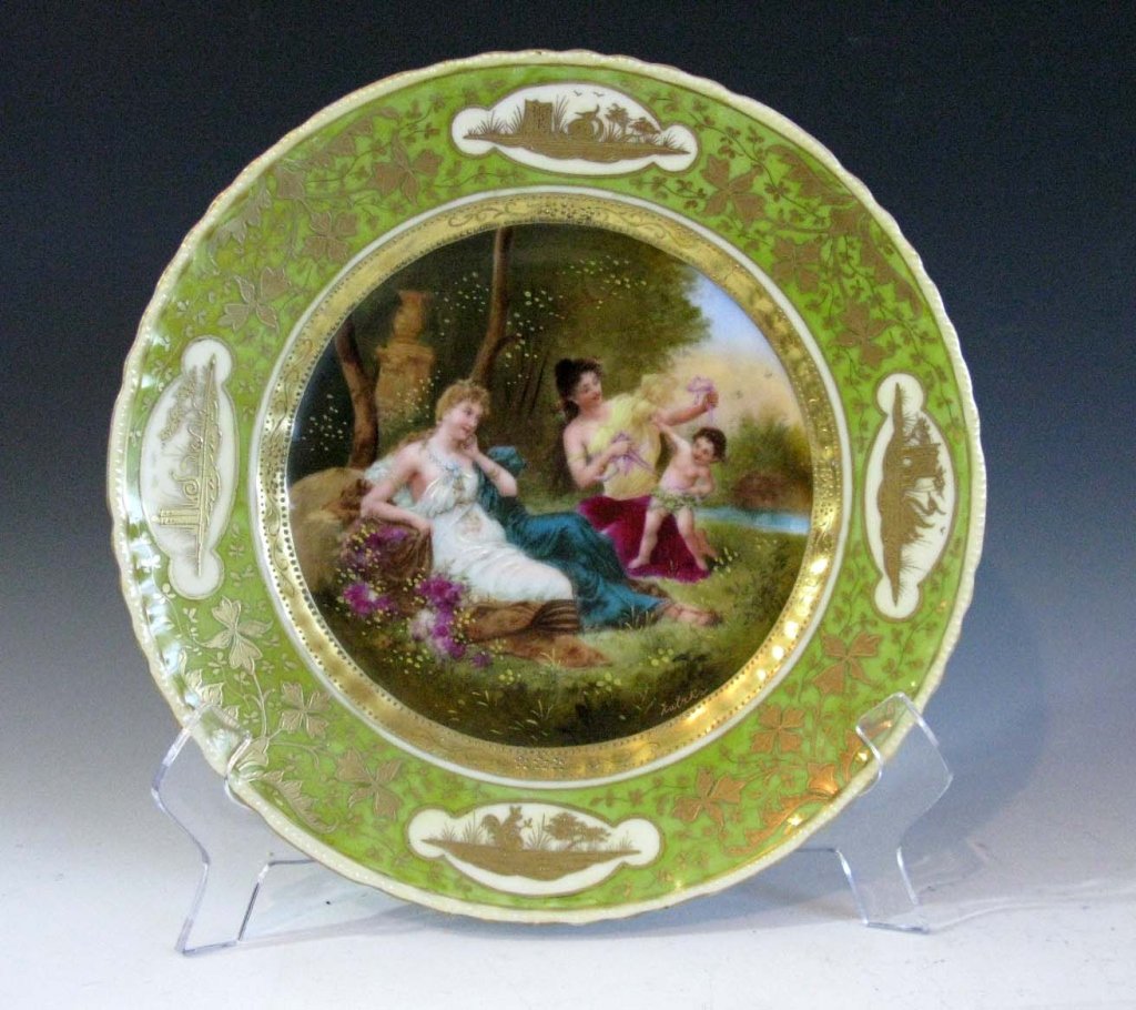 AUSTRIAN PAINTED AND GILDED PORTRAIT PLATE: AUSTRIAN PAINTED AND GILDED PORTRAIT PLATE: Titled, " A Little Capture," and depicting two women, catching cupid, hand painted and gilded over lithography, artist signed in gilding, 9.75"h.