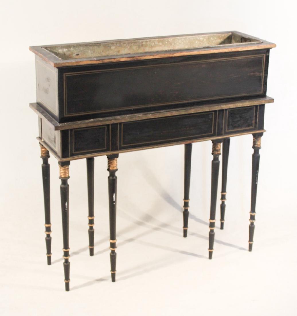 British Regency Style Planter or Wine Cooler: Late 19th century. Having rectangular form with black painted surface and gold trim, retaining metal liner at interior for plants or to chill wine, all resting on well turned and tapered legs. H39 1/2