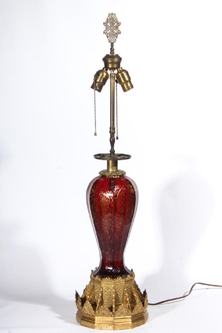 Antique Bohemian Glass & Gilt Bronze Table Lamp: Last half of the 19th century. Having a filigree finial above two light configuration continuing down to a well-cast gilt bronze collar continuing down the thick red glass chamber, which is handsomely