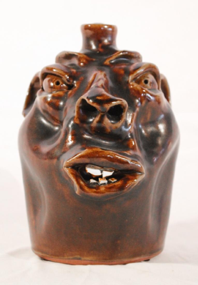Southern Stoneware Face Jug by Robert Brown: Circa 1980, Arden, North Carolina. The jug having a rich chocolate brown glaze with china teeth. Signed at the base. Good condition. H8 1/2"
