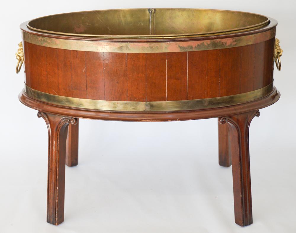 Very Fine George III Style Mahogany Wine Cooler: 20th century, England, by Wood and Hogan Inc. The piece has an excellent form with brass liner and bound brass construction boasting lion head handles atop four nicely shaped legs. H21" W30" D20"