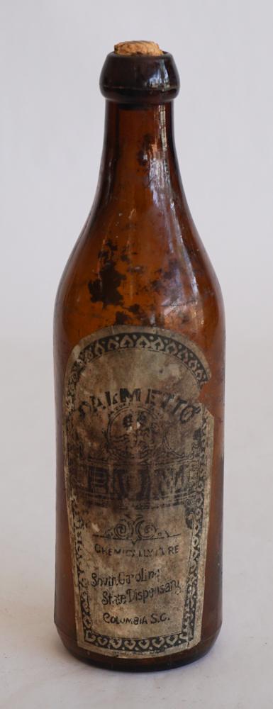 South Carolina Dispensary Paper Label Bottle: Antique Amber blob top bottled having original paper label for Palmetto Rum. Overall good condition, some discoloration consistent with age. No breaks or chips. H9 1/2" Sold from the collection of a G