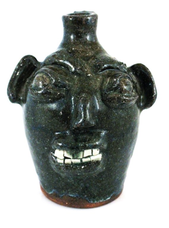 Southern stoneware face jug: Burlon Craig, Vale, North Carolina. circa 1970. Alkaline glazed face jug with slight rutle having relief decorated facial features and rare double-row broken china teeth. Stamped in base. H:7 1/2"