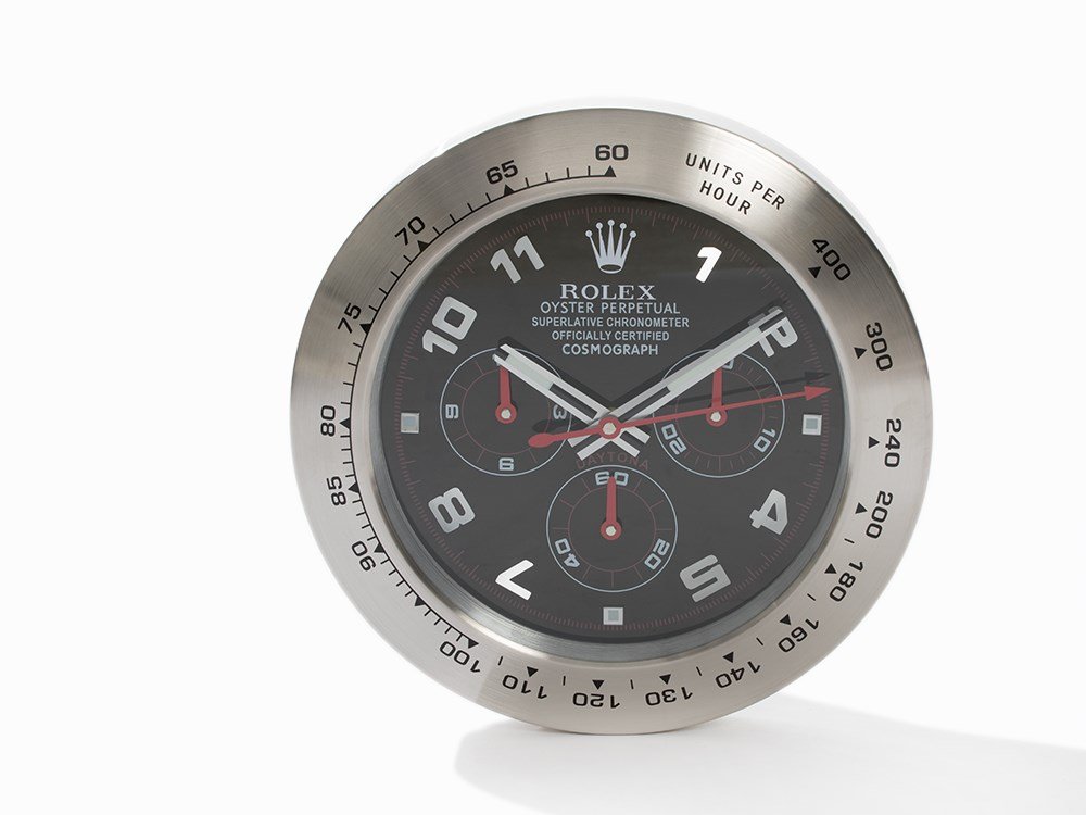 Wall Clock in Style of Rolex Daytona, c. 2015: Wall clock in style of Rolex Daytona c. 2015 Quartz movement, hour, minute, second Black dial, silver luminescent hands Watch case of steel Battery-driven Case diameter: c. 35 cm; Height: c. 5 cm Tota