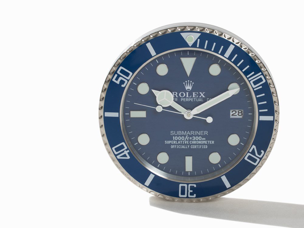 Wall Clock in Style of Rolex Submariner, c. 2015: Wall clock in style of Rolex Submariner c. 2015 Quartz movement, hour, minute, second, date Blue dial, silver luminescent Mercedes hands Watch case of steel Battery-driven Case diameter: c. 35 cm; Hei