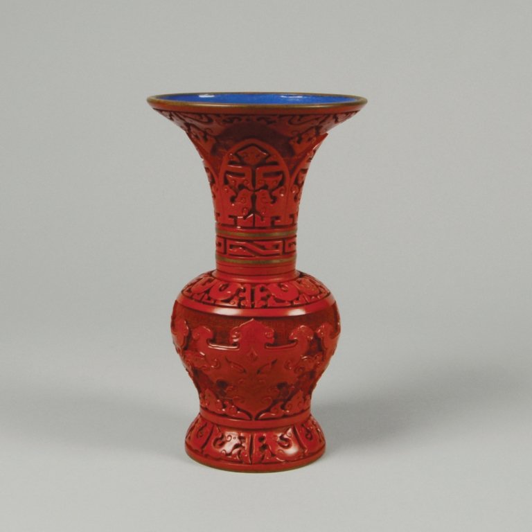 CARVED CINNABAR LACQUER VASE: Copper based. Two exposed copper rings on neck. Blue glazed base and interior. H: 8"