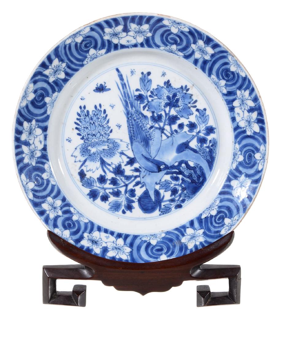 A Chinese blue and white plate , Kangxi, with a bird: A Chinese blue and white plate , Kangxi, with a bird perched on rockwork, painted with Kangxi six-character mark within double circle and of the period, 21cm diameter, wood stand Provenance: John Wall