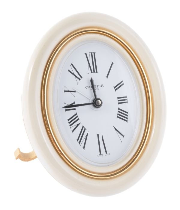 Cartier, an oval alarm clock, circa 2000, the crea: Cartier, an oval alarm clock, circa 2000, the cream lacquered bezel with gilt case, white dial, Roman numerals, blued hands, Cartier quartz movement cal. 289/235, with a fold out strut with C scroll f