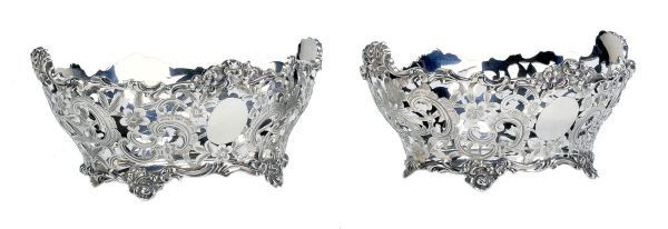A matched pair of silver oval sweet baskets, by Ch: A matched pair of silver oval sweet baskets, by Charles Stuart Harris, London 1899, and by Daniel and John Wellby, London 1905, with shaped floral and scroll rims, scroll engraved pierced bodies, on s