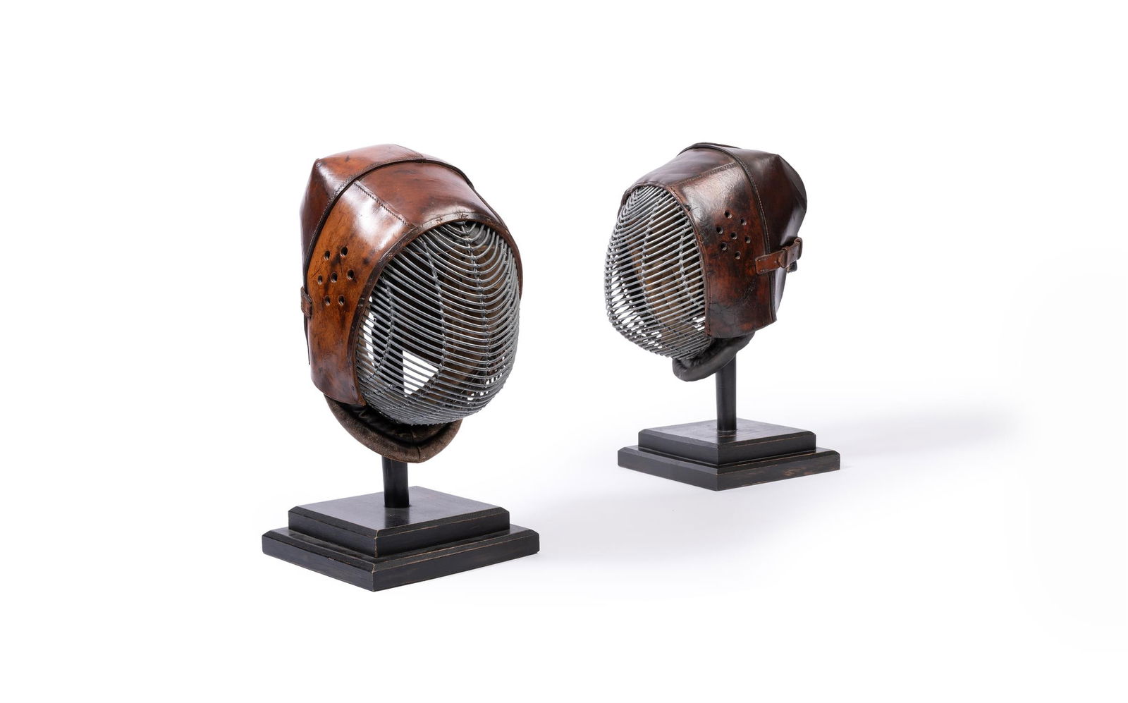 TWO LEATHER KENDO FENCING MASKS, JAPAN, EARLY 20TH CENTURY: TWO LEATHER KENDO FENCING MASKS JAPAN, EARLY 20TH CENTURY Each with iron grill plate, later ebonised turned stands approximately 42cm high overall, bases 24cm wide Provenance: Dreweatts 1759, Fine Fur