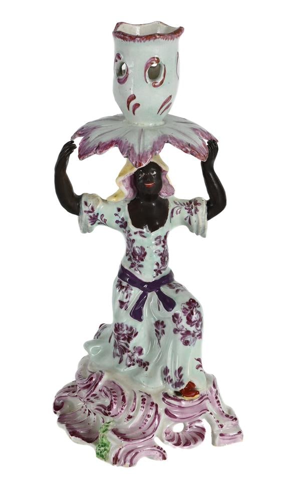 A BOW FIGURAL CANDLESTICK PROBABLY EMBLEMATIC OF AFRICA FROM A SERIES OF THE CONTINENTS, CIRCA 1760: A BOW FIGURAL CANDLESTICK PROBABLY EMBLEMATIC OF AFRICA FROM A SERIES OF THE CONTINENTS CIRCA 1760 Modelled kneeling supporting a sconce with leaf-shaped drip-pan 19cm high, 9cm at
