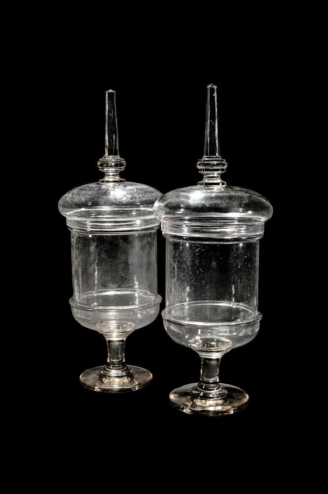 A PAIR OF CLEAR GLASS PEDESTAL CHEMIST JARS AND COVERS (1 of 2)