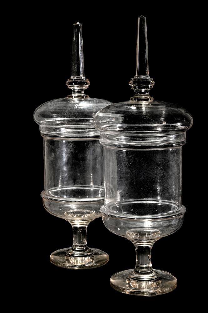 A PAIR OF CLEAR GLASS PEDESTAL CHEMIST JARS AND COVERS: A PAIR OF CLEAR GLASS PEDESTAL CHEMIST JARS AND COVERS With spire finials each 80cm high, 27cm diameter Condition Report: PLEASE NOTE: ALL LOTS ARE LOCATED AT SACKVILLE WEST STORAGE IN