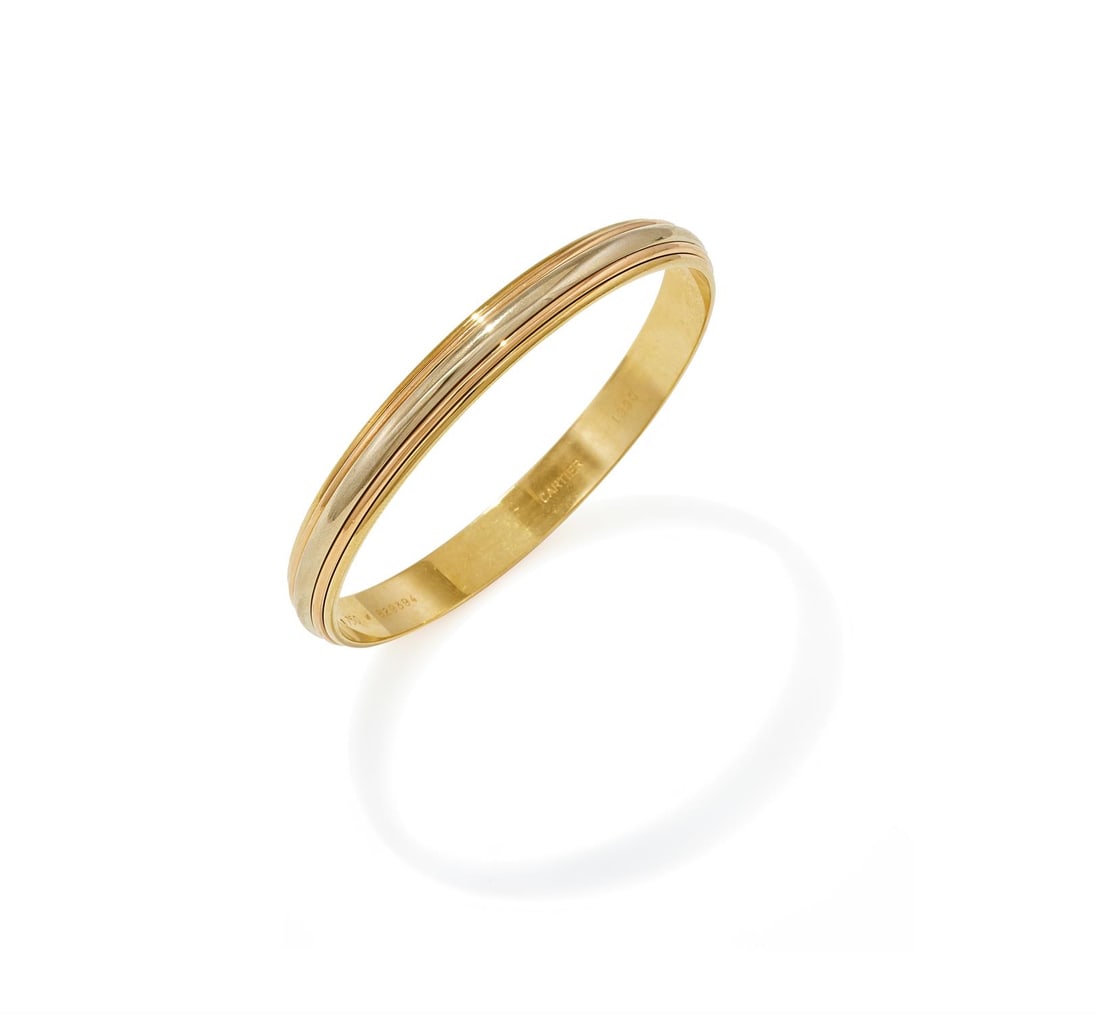 CARTIER, AN 18CT TRI-COLOURED GOLD BANGLE: CARTIER, AN 18CT TRI-COLOURED GOLD BANGLE Of stepped reeded tri-coloured gold design, signed Cartier, numbered B29394, maker's mark, with red maker's case and certificate of