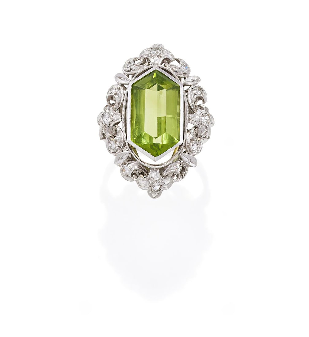 A MID 20TH CENTURY PERIDOT AND DIAMOND DRESS RING: A MID 20TH CENTURY PERIDOT AND DIAMOND DRESS RINGThe elongated octagonal cut peridot millegrain set within a pierced scrolled foliate surround set with single cut diamonds, stamped 18ct Size/dimension