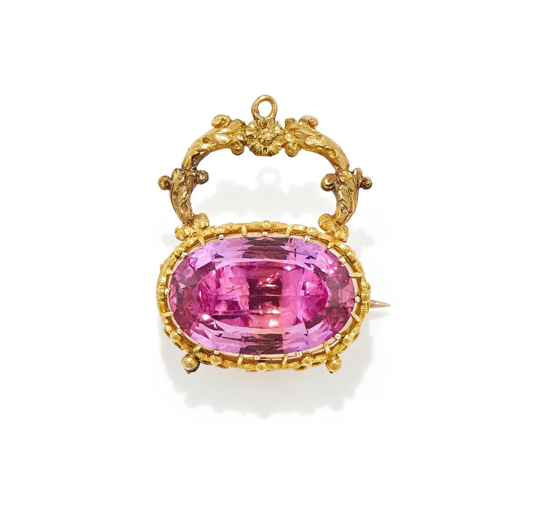 A REGENCY PINK TOPAZ BROOCH/PENDANT: A REGENCY PINK TOPAZ BROOCH/PENDANT CIRCA 1830 The oval cut pink topaz within a pink foiled back pinched collet setting, within a beaded textured wire setting with scrolled foliate and floral hoop, un