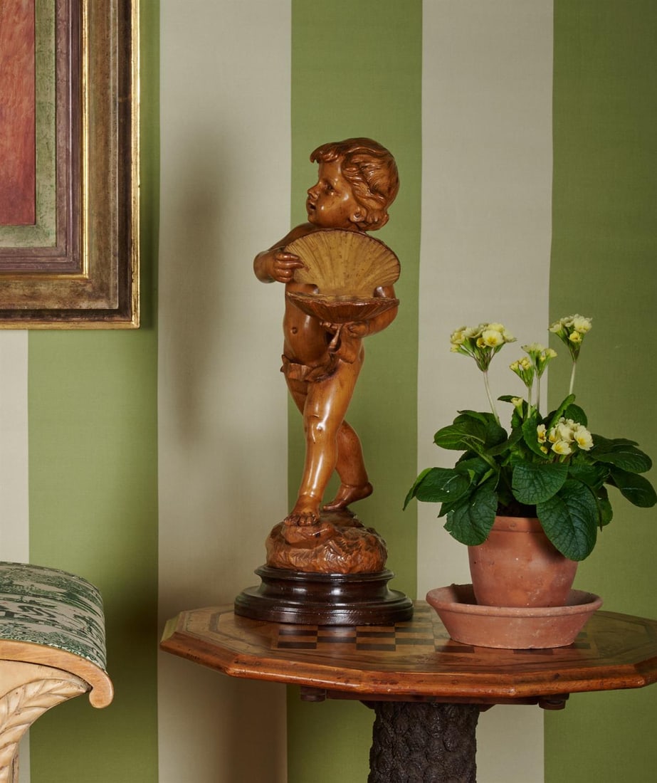 AN ITALIAN CARVED CYPRESS WOOD FIGURE OF A CHILD, 19TH CENTURY: AN ITALIAN CARVED CYPRESS WOOD FIGURE OF A CHILD 19TH CENTURY Depicted standing on naturalistic base holding a scallop shell, possibly a jewellery holder or lady's vide poche 51cm high