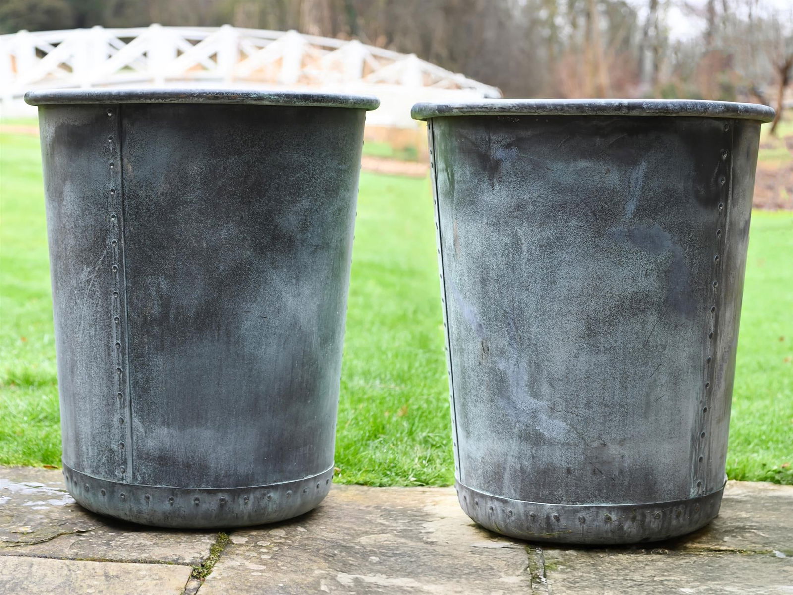 A PAIR OF PATINATED COPPER AND RIVETED CIRCULAR PLANTERS: A PAIR OF PATINATED COPPER AND RIVETED CIRCULAR PLANTERSWith a rollover edge, tapering cylindrical body, pierced for drainage76cm high, 66cm diameter