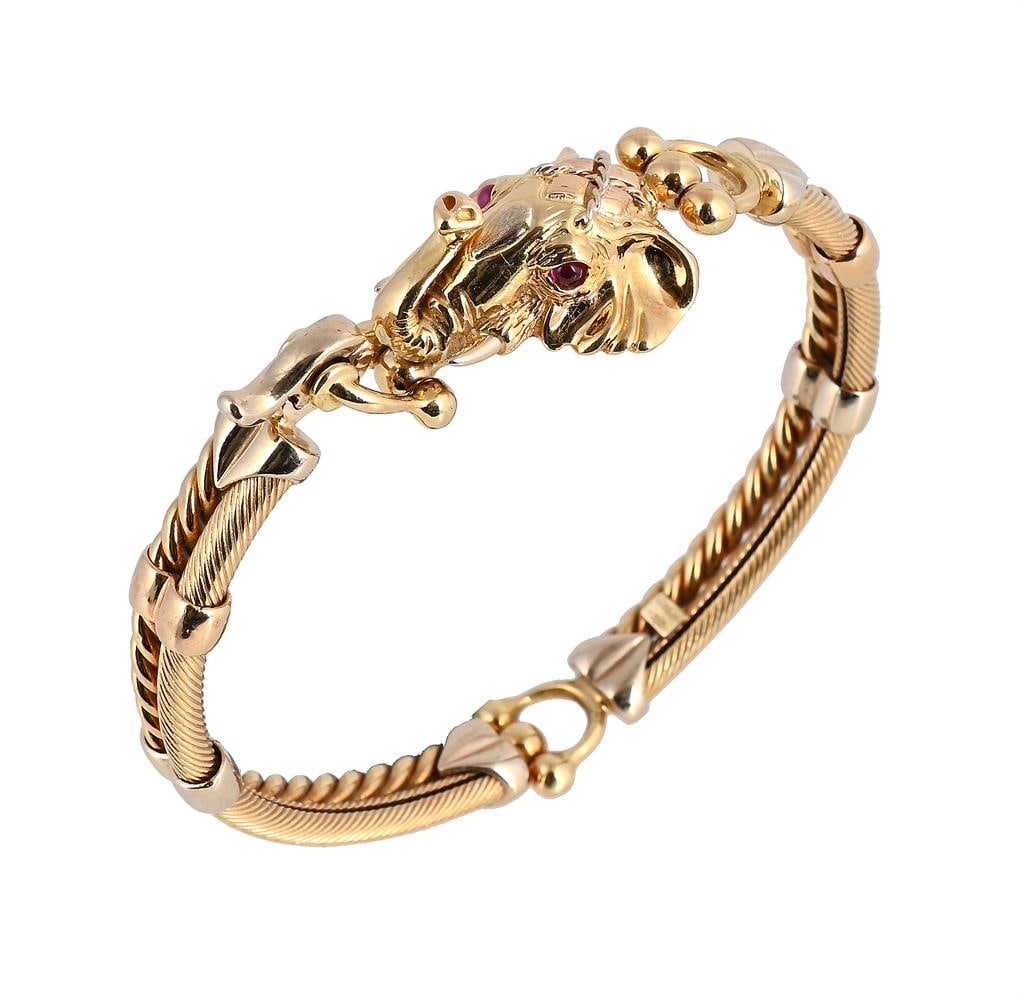 AN ELEPHANT BANGLE: AN ELEPHANT BANGLE The elephants head with circular cabochon pink stone eyes, to polished and ropetwist linked sections, stamped 750 with Italian control mark Size/dimensions: inner