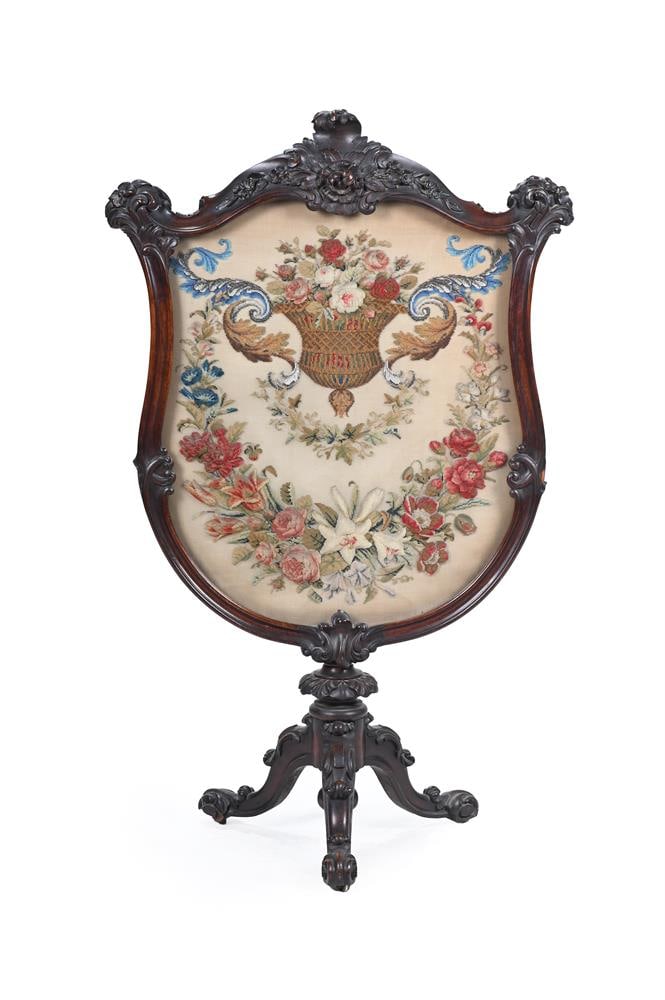 Y A VICTORIAN INDIAN ROSEWOOD TRIPOD SCREEN, CIRCA 1865: Y A VICTORIAN INDIAN ROSEWOOD TRIPOD SCREEN CIRCA 1865 Shield shape frame carved rococo flower sprays, stiff leaf low pedestal on scroll carved base, panel embroidered in gros point, stump work
