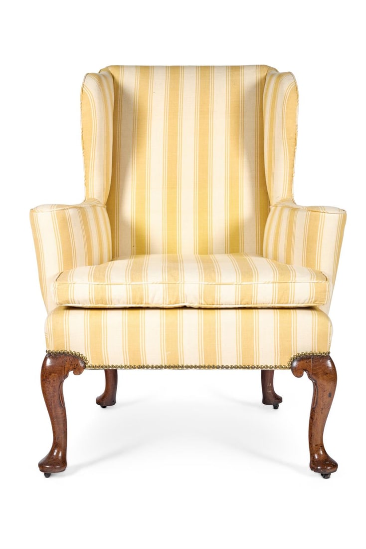 A GEORGE II WALNUT WING ARMCHAIR, CIRCA 1730: A GEORGE II WALNUT WING ARMCHAIRCIRCA 1730Of typical form with scrolled arms and a loose cushion upholstered in yellow striped covers on scrolled cabriole legs with pad feet and leather castors, part-