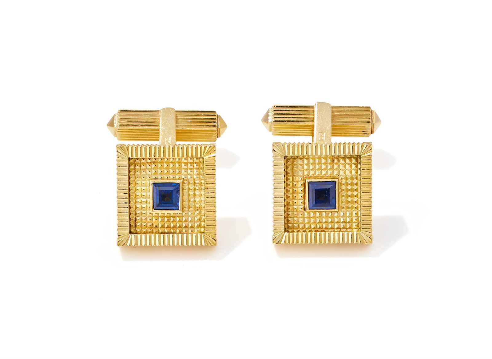 CARTIER, A PAIR OF SAPPHIRE SET CUFFLINKS: CARTIER, A PAIR OF SAPPHIRE SET CUFFLINKSCIRCA 1970Each square 18ct gold panel of reeded and hobnail design, collet set with a square cut sapphire, to reeded baton terminals, numbered N9874, UK import