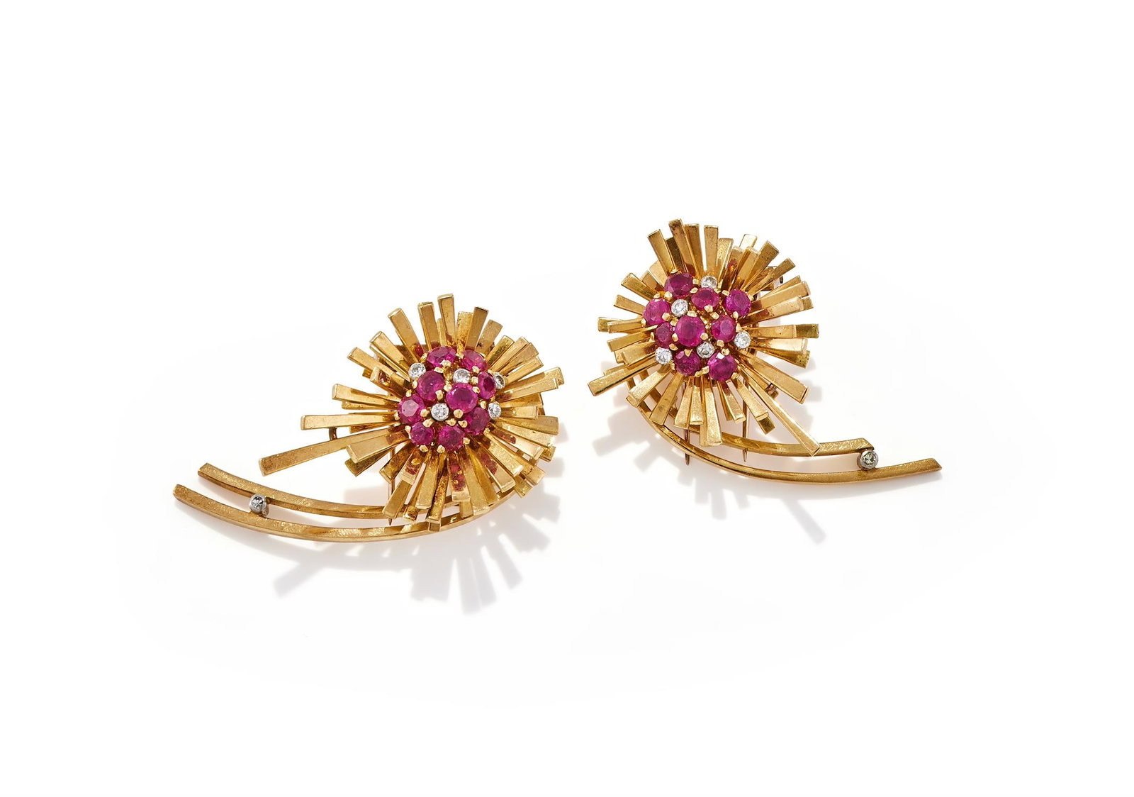 A PAIR OF RETRO RUBY AND DIAMOND CLIP BROOCHES: A PAIR OF RETRO RUBY AND DIAMOND CLIP BROOCHESOf opposing design, each circular cut ruby and diamond cluster within a radiating surround of tapered polished spokes with a single diamond accent, twin p