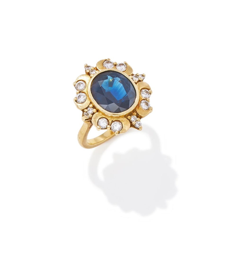 BOODLE AND DUNTHORNE, A SAPPHIRE AND DIAMOND CLUSTER RING: BOODLE AND DUNTHORNE, A SAPPHIRE AND DIAMOND CLUSTER RINGLONDON, 1993The oval cut sapphire collet set within a surround set with brilliant cut diamonds between crescent shaped spacers, mounted in