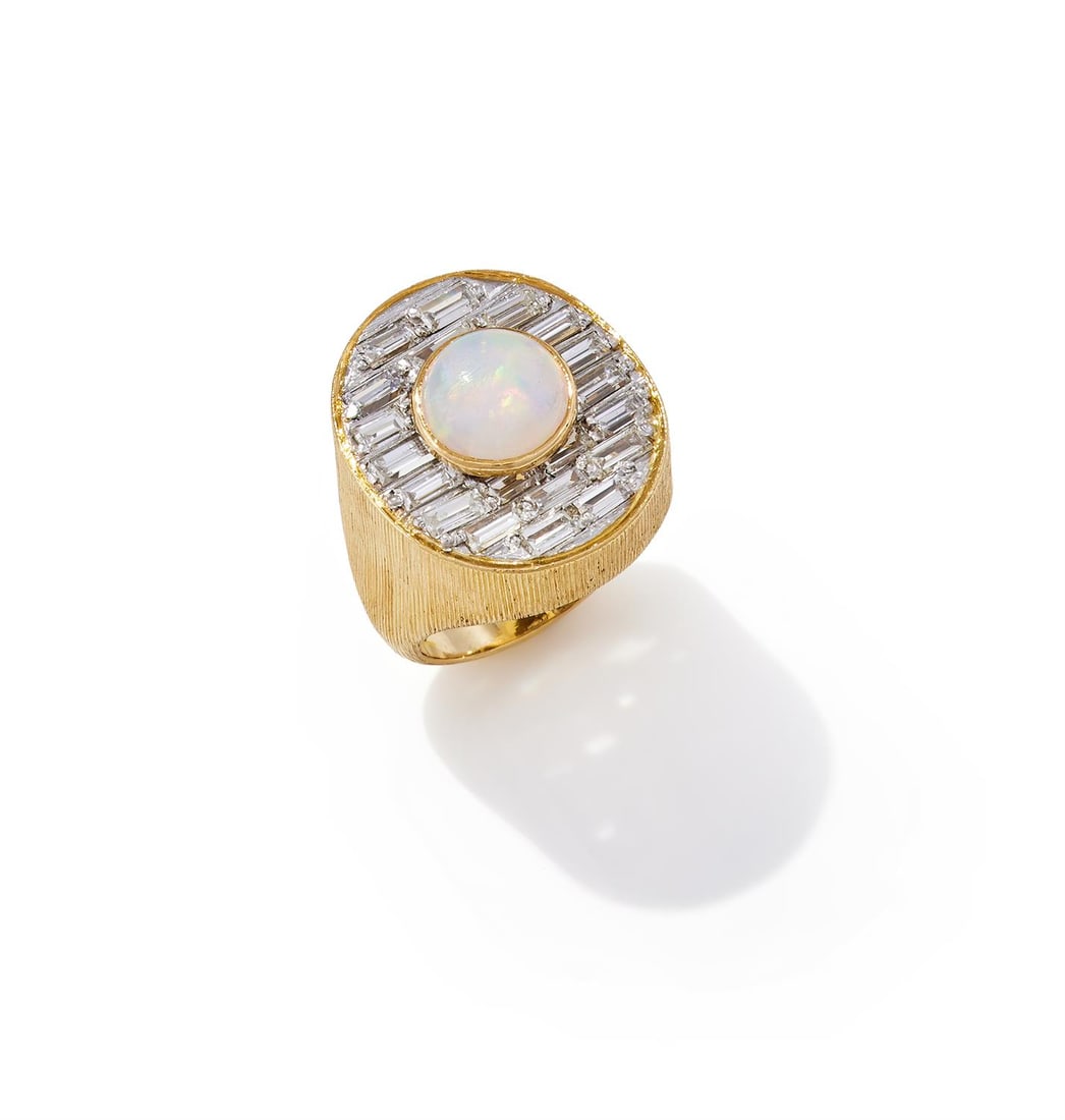 ANN SOPHIA MADELINE BUZZARD, AN OPAL AND DIAMOND DRESS RING: ANN SOPHIA MADELINE BUZZARD, AN OPAL AND DIAMOND DRESS RING LONDON, 1972The oval panel collet set with a circular cabochon opal, within a baguette cut diamond surround, in a raised mount of reeded