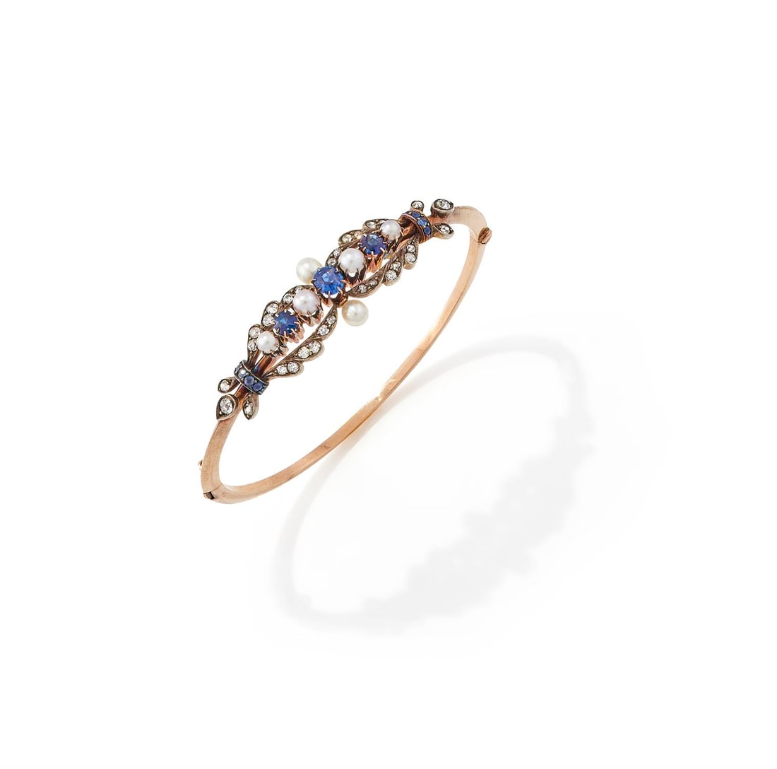 A LATE 19TH CENTURY SAPPHIRE, PEARL AND DIAMOND BANGLE: A LATE 19TH CENTURY SAPPHIRE, PEARL AND DIAMOND BANGLEThe hinged bangle set with a raised row of alternating sapphires and half pearls, within an old European cut diamond spray surround with sapphire 
