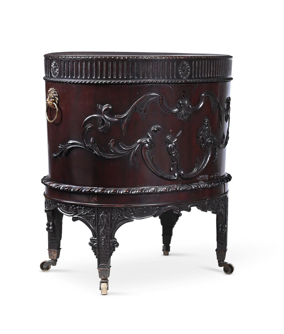 A CARVED MAHOGANY AND GILT METAL MOUNTED OVAL WINE COOLER, IN GEORGE III STYLE, 19TH CENTURY: A CARVED MAHOGANY AND GILT METAL MOUNTED OVAL WINE COOLERIN GEORGE III STYLE, 19TH CENTURYThe hinged cover enclosing a lead lined interior with a central drain and stopper63cm high, 57cm wide, 43cm de