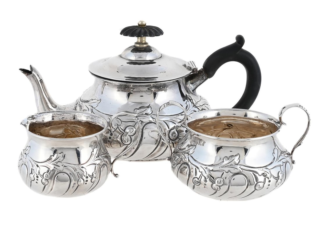 AN EDWARDIAN SILVER THREE PIECE BACHELOR'S TEA SET: AN EDWARDIAN SILVER THREE PIECE BACHELOR'S TEA SET CHARLES EDWARDS, LONDON 1904 The tea pot with a wood lobed oval finial and loop handle, the half lobed baluster body with a vine band 21cm long