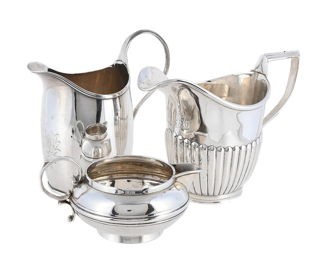 THREEE SILVER MILK JUGS: A GEORGE III SILVER OVAL MILK JUG MAKER'S MARK OBSCURED, LONDON 1796 With a reeded border and scroll handle, engraved with a monogram within a foliate reserve 11.5cm high Together with: A SILVER