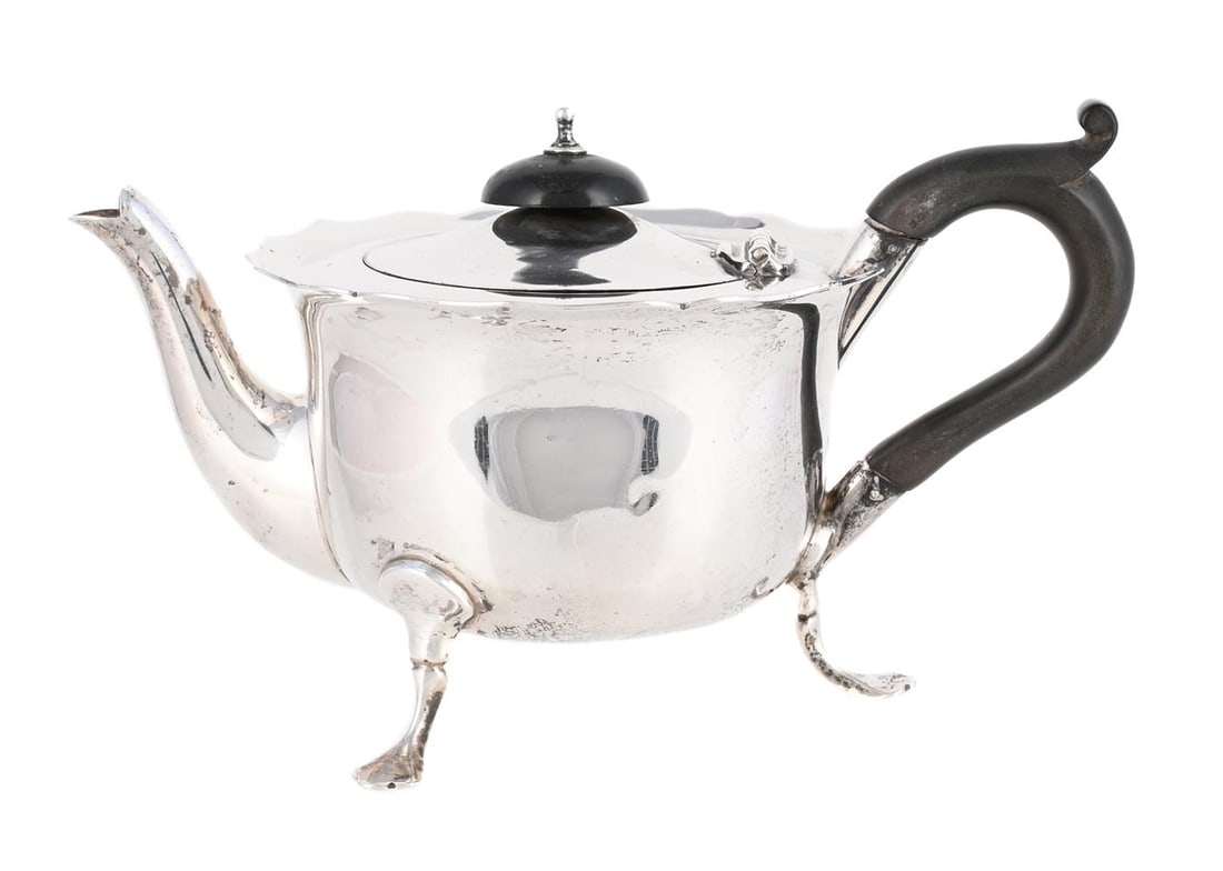 A SILVER SHAPED CIRCULAR BACHELOR'S TEAPOT: A SILVER SHAPED CIRCULAR BACHELOR'S TEAPOT GEORGE UNITE & SONS, BIRMINGHAM 1927 With a wood domed finial and scroll handle, shaped border and on three trefoil feet 18.5cm long 238g (7.65 oz)