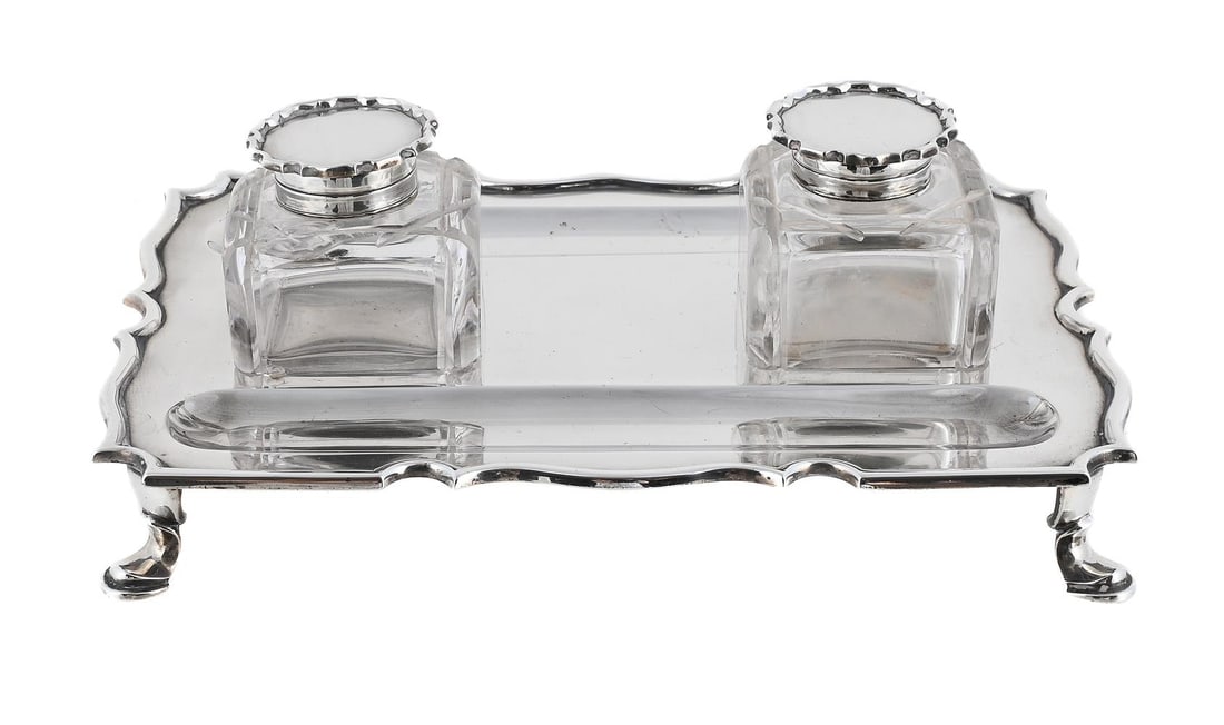 A SILVER SHAPED RECTANGULAR INKSTAND: A SILVER SHAPED RECTANGULAR INKSTAND C. S. HARRIS & SONS LTD., LONDON 1924 With a shaped border. two pen wells and on four pad feet 22cm long Together with: TWO SILVER MOUNTED AND GLASS INKWELLS